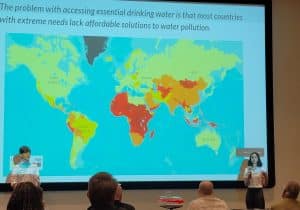 Zoe Darshan starting Dew Drop Presentation. World map behind her as she presents to judges in crowd.