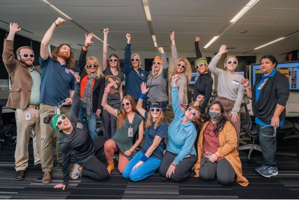 A group of people from the OT department wearing party glasses with hands in the air