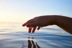 Hand tapping water creating ripples with sunlight in the background