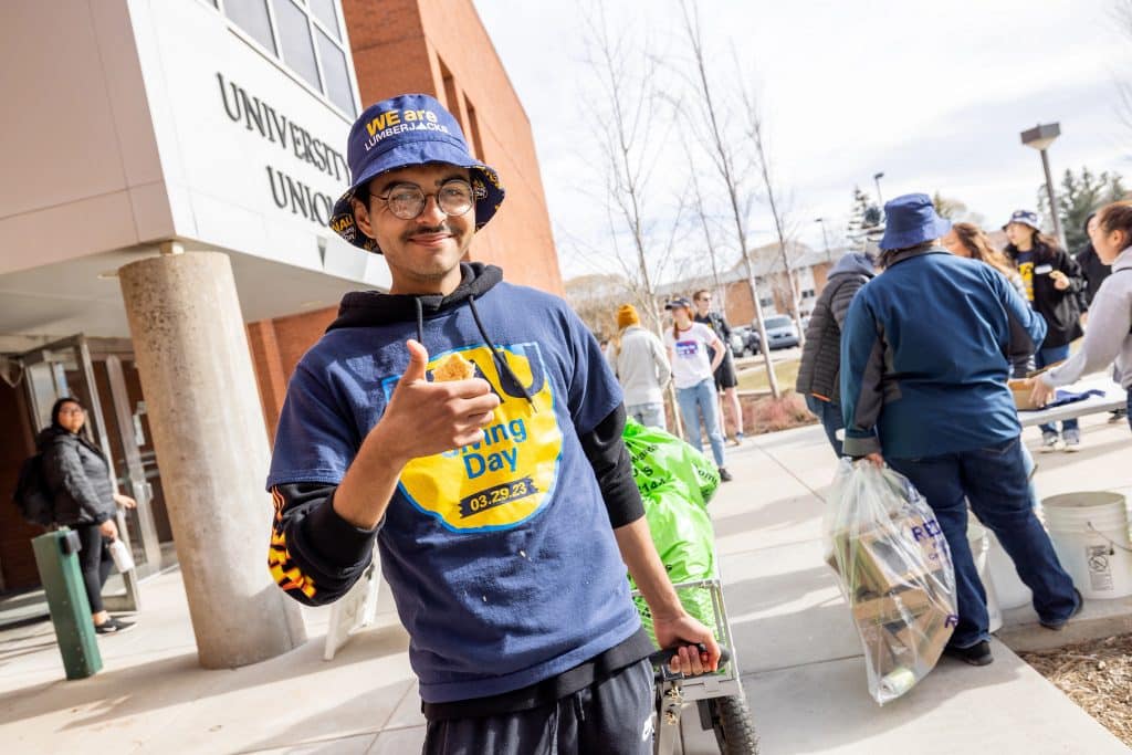 A student in a Giving Day shirt gives a thumbs up.
