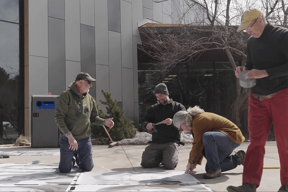 People tape pictures to the sidewalk as part of the People's Art Project