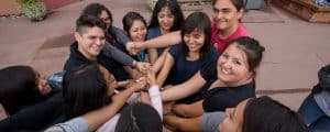 A group of Native American students stand in a circle with their hands in the middle