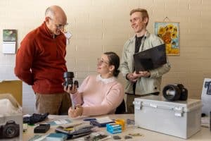 Three people sit at a desk with equipment