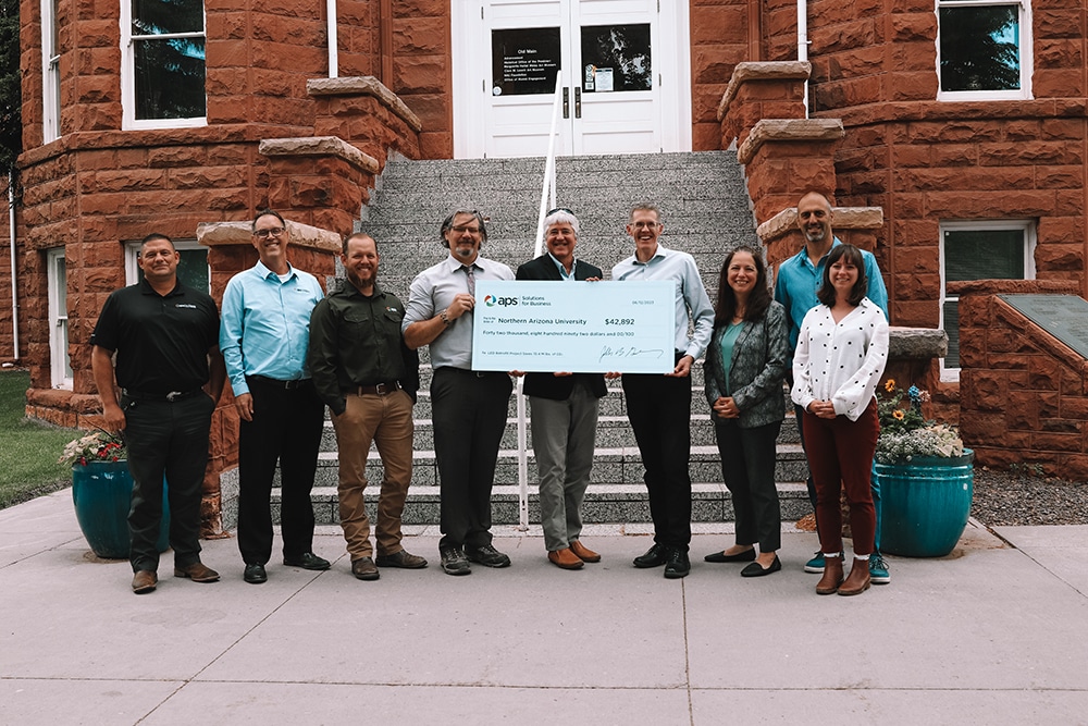 Seven people hold a big check in front of the staircase at Old Main
