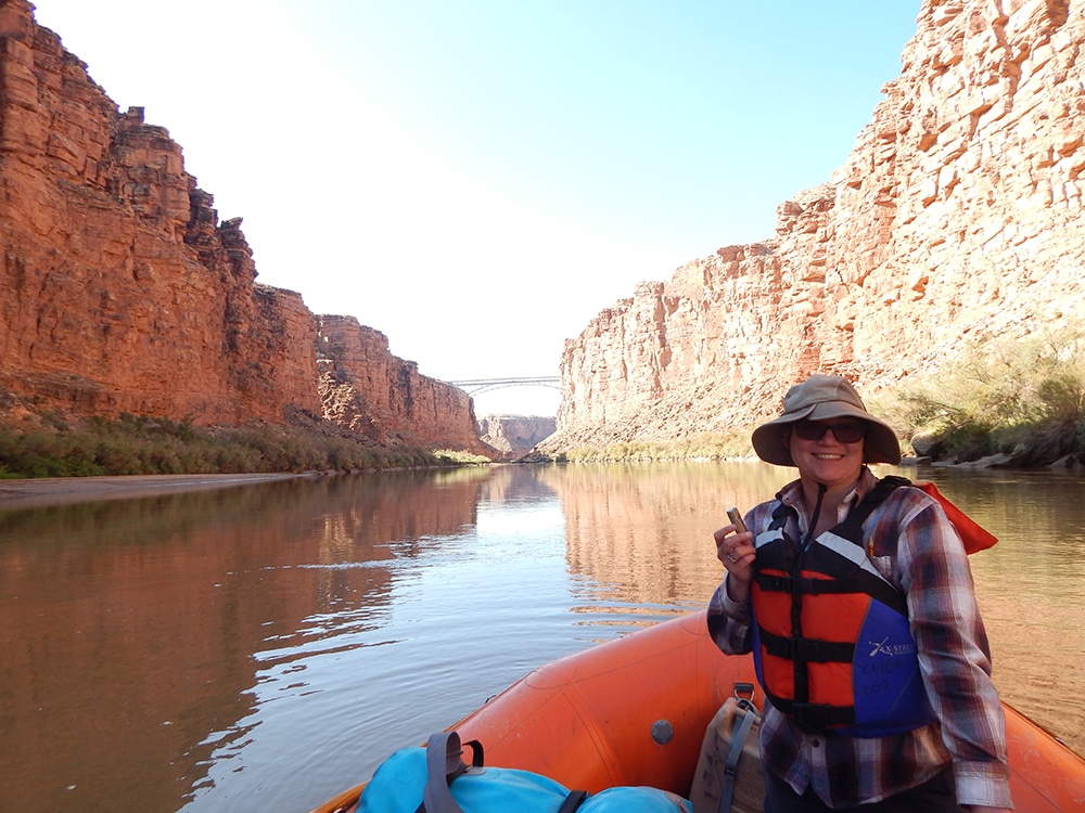 Melissa Sevigny on a raft in the middle of the Colorado River in the Grand Canyon with a bridge in the background