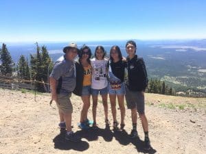 Patty Diaz and her family stand on a trail on top of a mountain with blue sky.