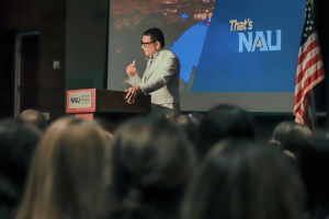 President Cruz Rivera stands on the stage in front of a slide that says NAU