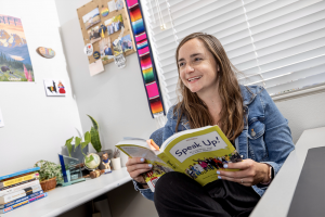 McKenzie McLoughlin in her office holding a book with other books on the desk.