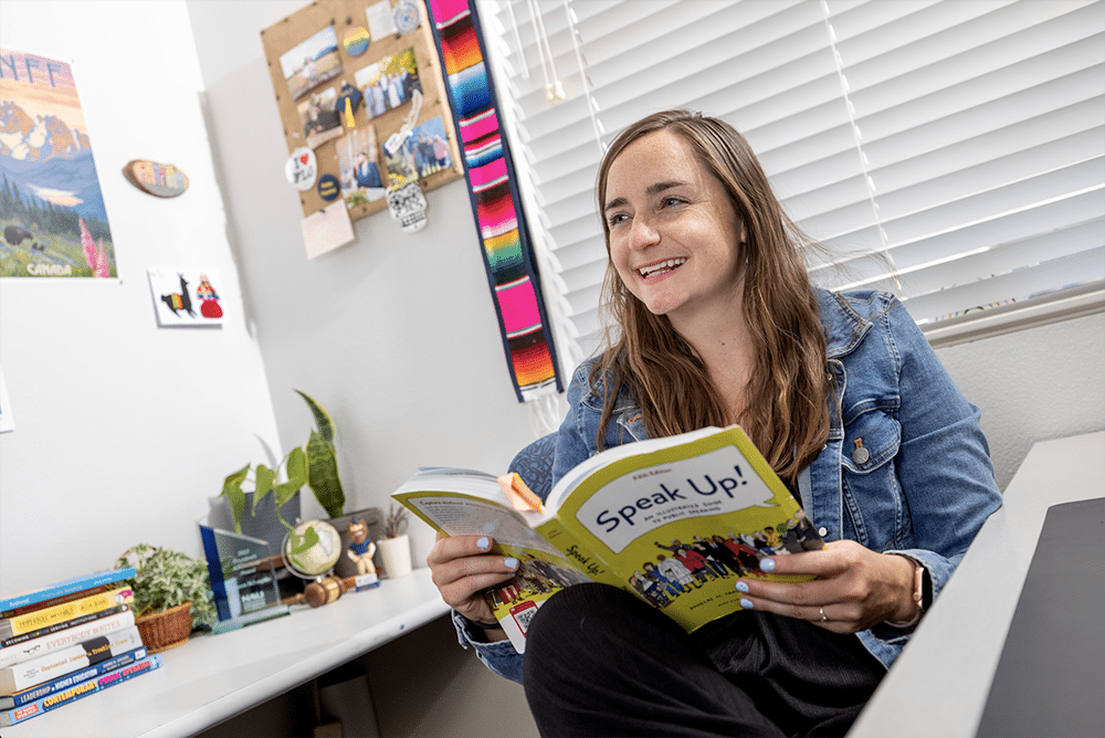 McKenzie McLoughlin in her office holding a book with other books on the desk.