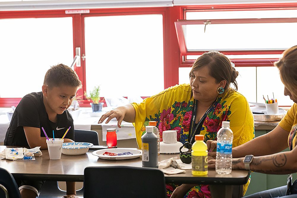 A student and teacher mix paints on a classroom table.