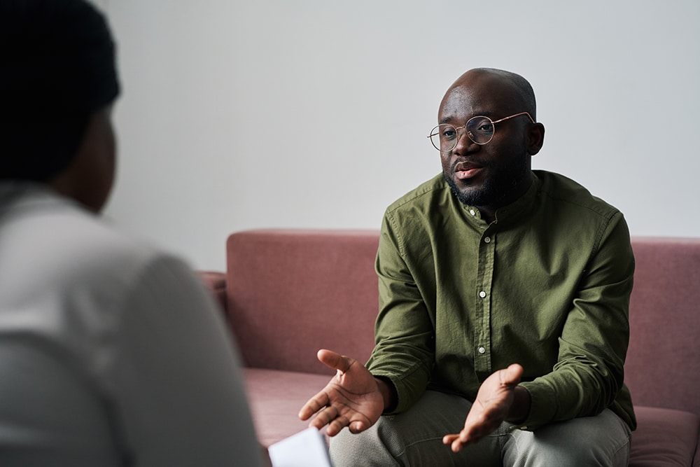 Young black man in casualwear sitting on couch during talk with therapist