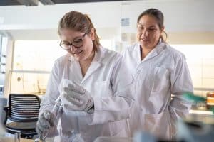 Chemistry professor Naomi Lee wearing a white lab coat helping a student wearing a white lab coat.