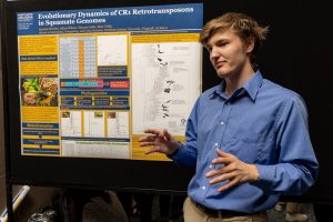 A student stands by his poster about informatics research and talks to people about his work.