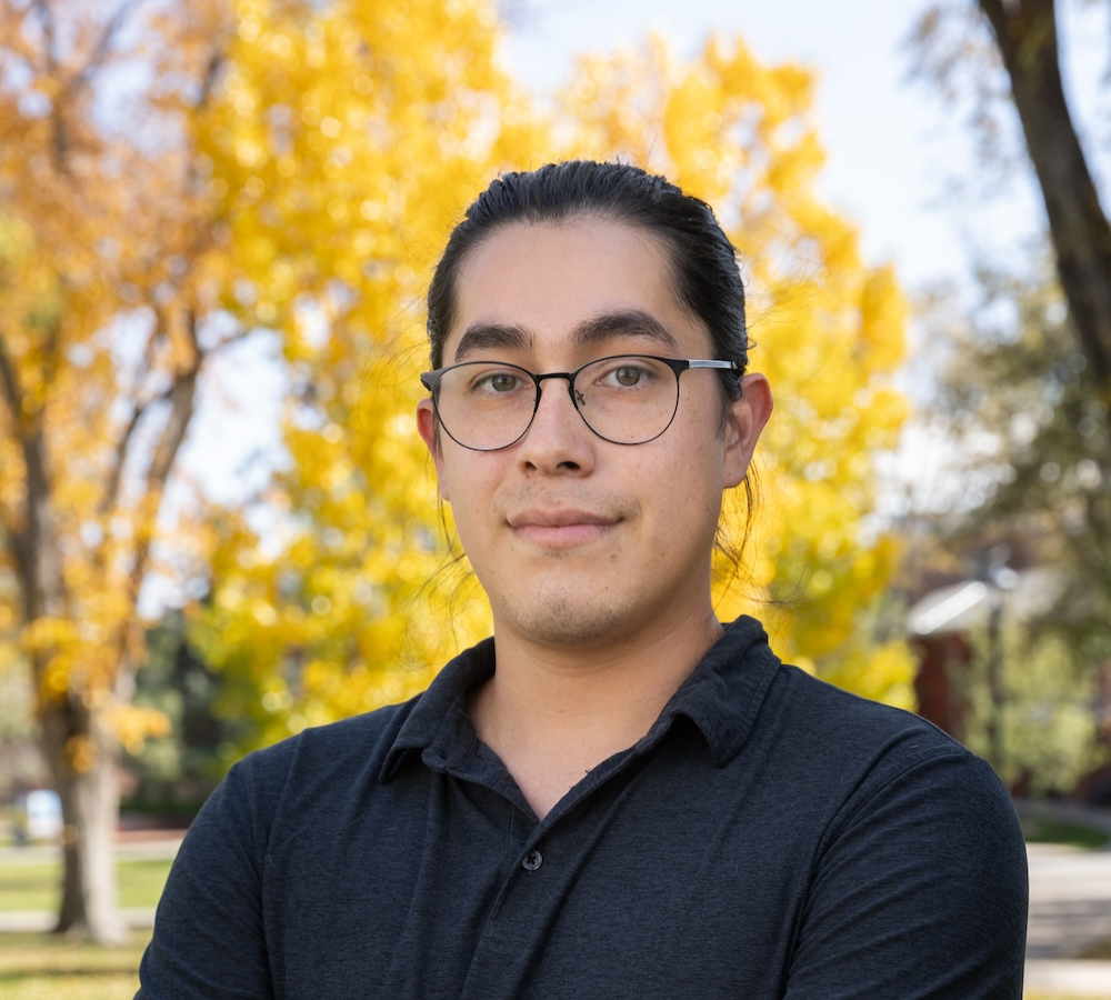 Daniel Kennedy standing with arms crossed wearing a black shirt with gold aspen trees in background