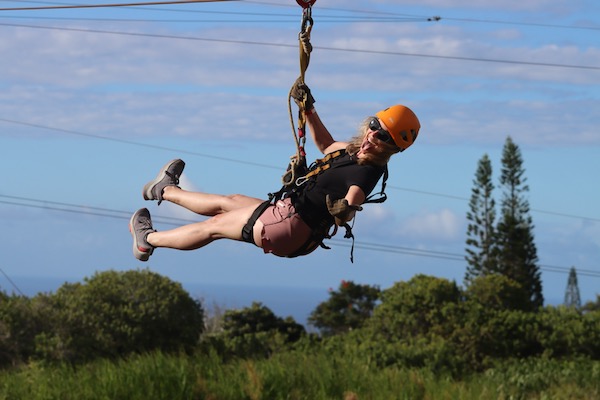 Ali Applin on a zipline with blue sky and forests in the background