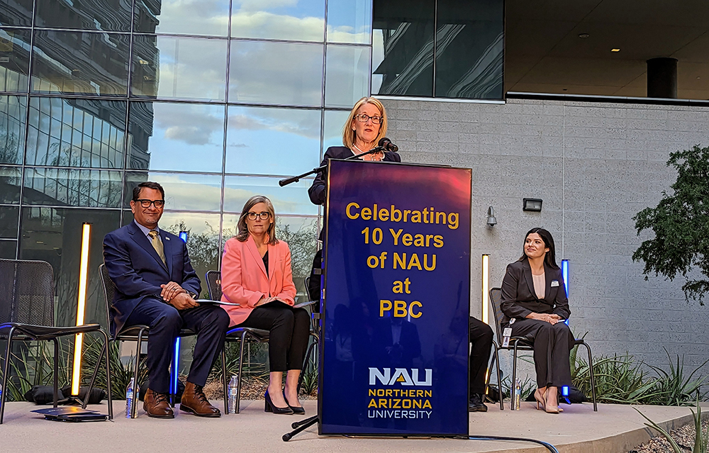 Christy Farley at a dais with NAU President José Luis Cruz Rivera and Arizona Gov. Katie Hobbs sitting behind her.
