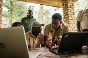 Community scientists in an open-air ramada with open laptop computers on the table in front of them.