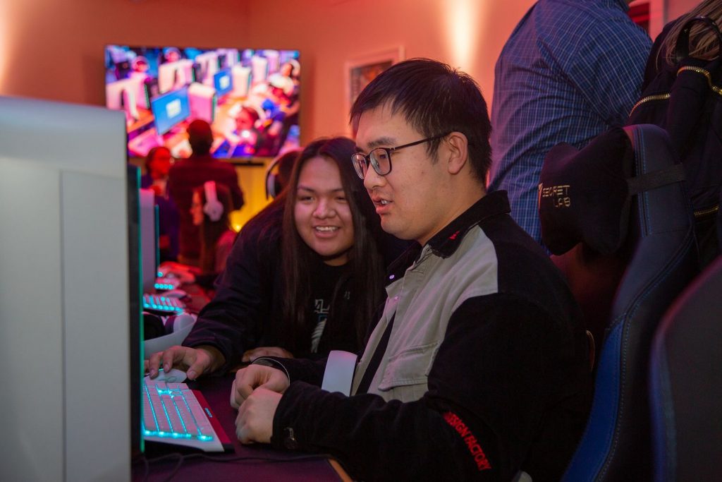 two students smiling as they look at a computer screen in the Advanced Media Lab at NAU