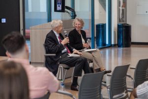Tom Petri and Karan English speaking into microphones while sitting in chairs in front of an audience