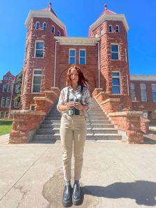 Victoria Wiley holding binoculars in front of Old Main on the NAU campus