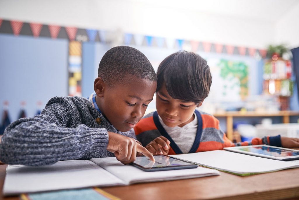 Two children looking at a tablet while sitting together in an elementary school classroom