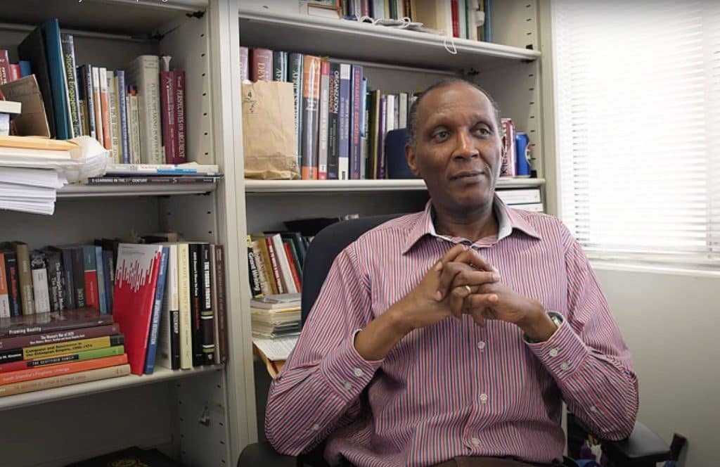 Ishmael Munene sitting in his office in front of a large bookshelf