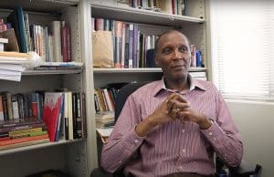 Ishmael Munene sitting in his office in front of a large bookshelf