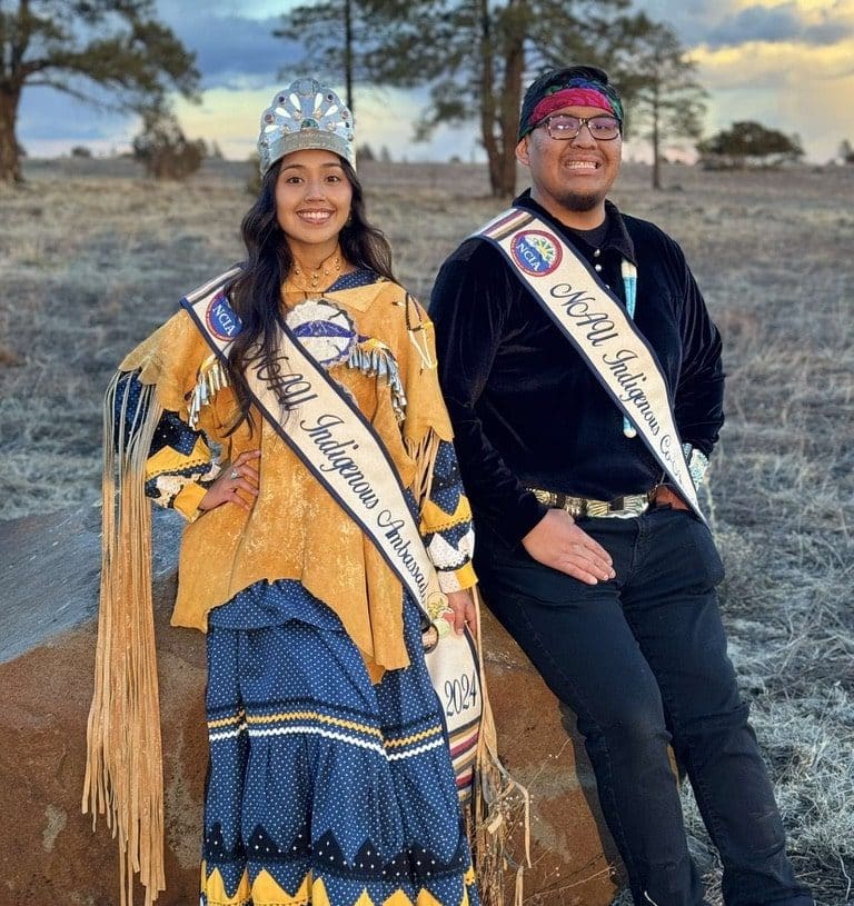 2024 Indigenous Ambassador Báásè Pike and co-ambassador Denver Seaton pose outdoors with their honorary club sashes.