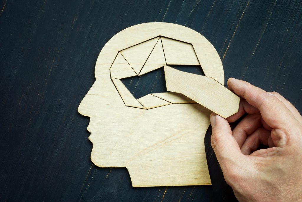 hand putting a missing piece inside a wooden puzzle in the shape of a brain