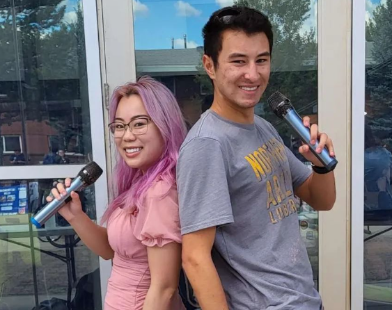 NAU Karaoke Club President Cameron Eickhoff and Vice President Joey Tse pose back-to-back with microphones at an NAU club fair.