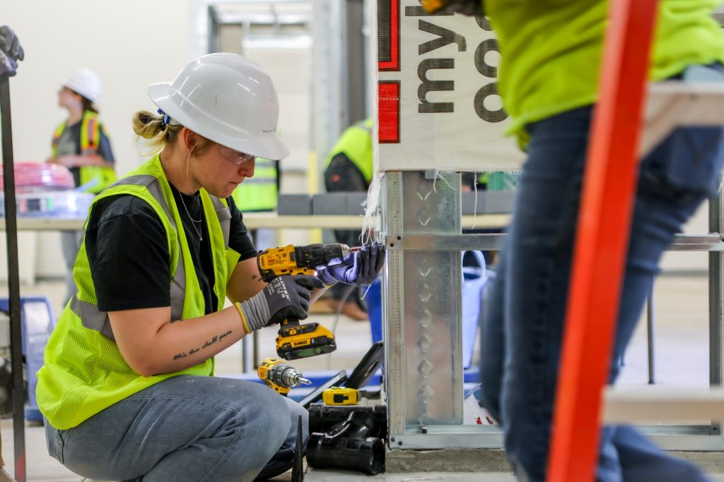 A construction management student uses a drill in the bathroom she's helping build.
