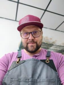 Selfie of Nic Beckett wearing a pink hat and T-shirt with a gray apron