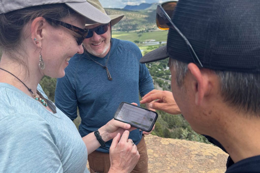 Three people using the new TWIG platform on a smartphone while outside in Flagstaff
