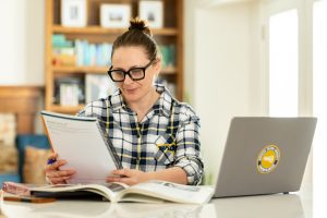 Woman reading a notebook with a laptop next to her