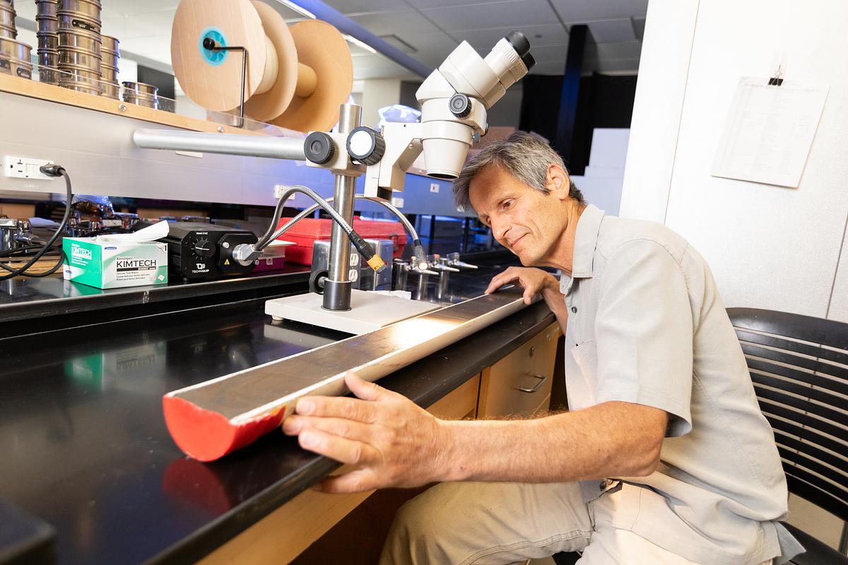 An older person wearing a light-colored shirt and standing in a laboratory setting, interacting with scientific equipment and devices on a counter.