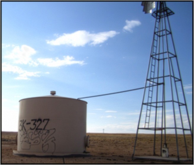 A large concrete water well sits on desert land adjacent to a windmill.