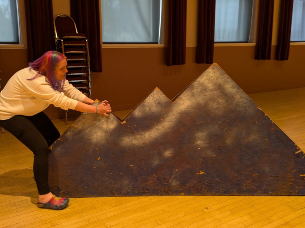 Stephanne moving a stage prop that looks like mountains.