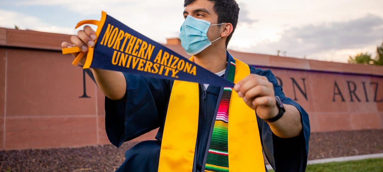 Graduate with mask, stole, and a NAU pennant